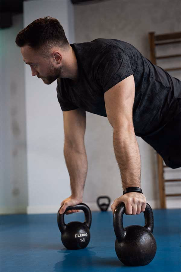Mężczyzna ćwiczący w podporze na kettlebells w klubie Quantum Fitness